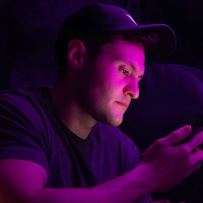 Chris Withers in a cap, face lit magenta by a phone screen in the dark